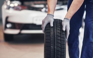 Mitarbeiter rollt einen Reifen vor einem Auto in einer Werkstatt.