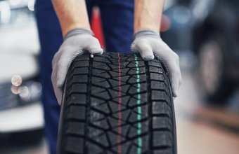 Eine Person trägt graue Handschuhe und hält einen schwarzen Autoreifen mit farbigen Profilmarkierungen.