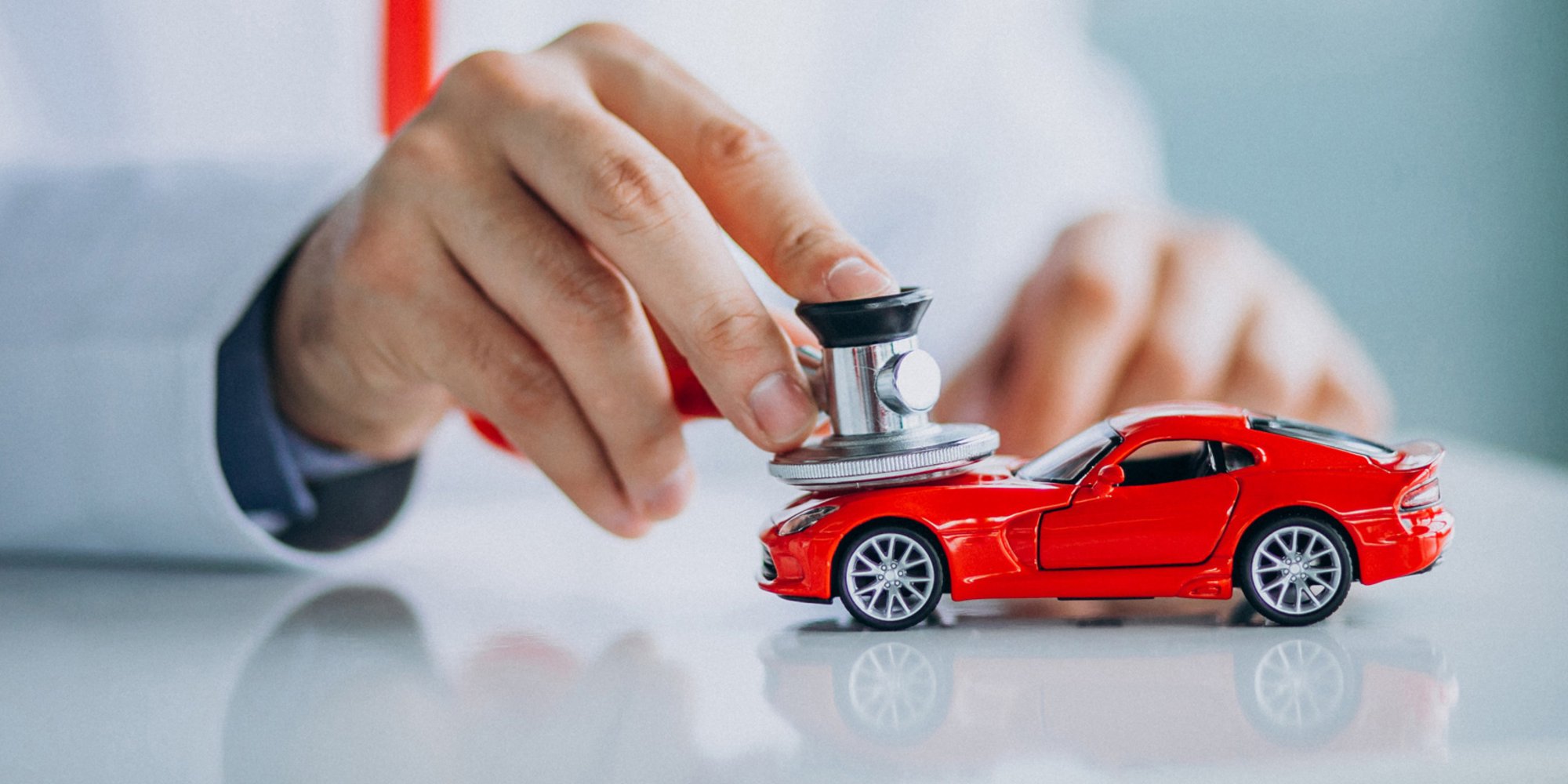 Person untersucht ein rotes Spielzeugauto mit einem Stethoskop – symbolisch für eine Fahrzeugdiagnose.